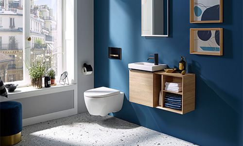 Ein Ausschnitt von einem Badezimmer mit einer blauen Wand. Im Fokus eine Toilette mit Wandhalterung und ein Waschtisch mit Spiegel.